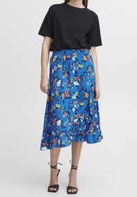 Blommig ankellång kjol i blått tyg med flerfärgade blommor, med volangkant och elastisk midjeband, kombinerad med en svart t-shirt.