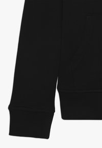 Černá bavlněná mikina s ribovanými manžetami a klokaní kapsou na přední straně. Hladká textilie s minimálním detailováním švů.