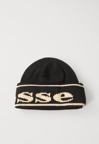 Svart strikket lue med en bred kremfarget stripe som har ordet "SSE" i en fet, stilisert skrifttype. Myk tekstur, enkelt design og tett passform.