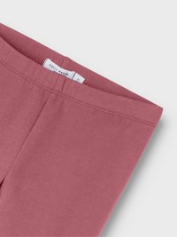 Leggings en coton rose avec une texture lisse, une taille élastique et une étiquette indiquant "besoins essentiels" à l'intérieur. Design simple, sans motifs.