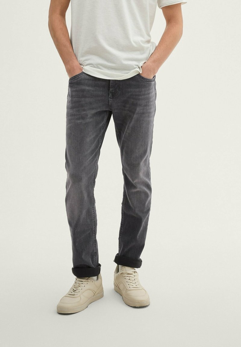 Gray denim jeans with a slim fit, featuring faded detailing. Paired with light beige sneakers, rolling at the ankles.