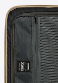 Interno di una valigia rigida con un tessuto scuro e strutturato, numerosi scomparti zip, sezioni in rete e un'etichetta di marca.