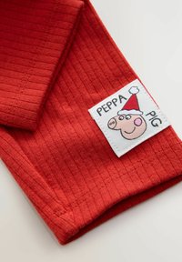 Rød ribbet stof med en syet hvid label, der viser en tegneseriegris iført en rød hat, mærket "PEPPA PIG." Blød tekstur og lys farve.