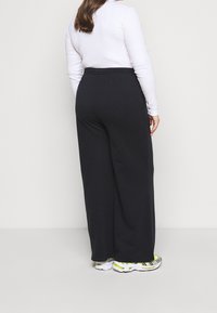 Svarta vida byxor med elastisk midja, tillverkade av ett mjukt material. Kombineras med vita sneakers med neondetaljer.