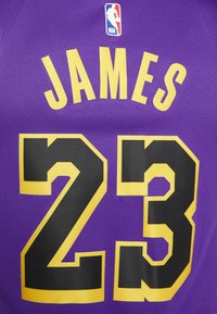 Lila baskettröja med stora svarta siffror "23" och namnet "JAMES" i gult. NBA-logotypen i det övre vänstra hörnet.