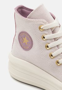 Purple canvas high-top sneaker featuring gold eyelets, white laces, and a circular emblem with a yellow star on the side.