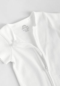 Hvid ribbet baby romper med korte ærmer, der har en frontlynlås og blødt stof. Etiketten er synlig med mærkenavn og plejevejledninger.