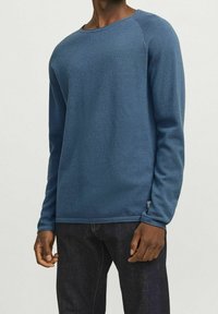 Blå långärmad tröja i strukturerad stickad material, med rundhals och ribbad mudd, kombinerad med mörka jeans.