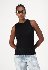 Top negro sin mangas con un cuello redondo. Textura suave. Combinado con unos vaqueros de serpiente de color azul claro. Los accesorios incluyen gafas de sol y pendientes.