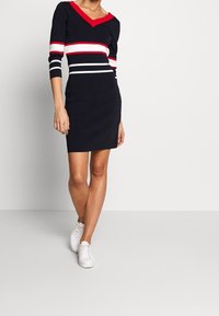 Granatowa sukienka z dekoltem w serek, z czerwono-białymi poziomymi paskami na torsie i rękawach. Wykonana z elastycznego materiału, długość do kolan.