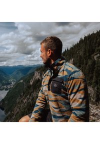 Sudadera de forro polar en azul, oliva y rayas de tigre naranjas, con cuello de media cremallera y bolsillo frontal negro. Tejido texturizado y cálido.