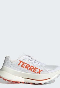 Chaussure de course Terrex blanche et orange avec une semelle épaisse et une semelle extérieure texturée, vue de côté sur un fond clair.