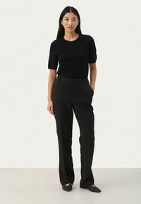 Must mustreeritud must lühikeste varrukatega topp, mis on seotud kõrge vöökohaga mustade pükstega. Riietus on elegantse ja kohandatud disainiga ning sileda tekstuuriga.