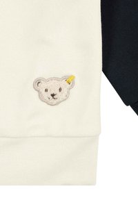 Katoenen sweatshirt met een crèmekleurige voorkant en marineblauwe mouwen. Heeft een textuur en een geborduurde berenkop met een gele accentspeld.
