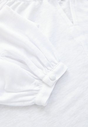 Manșetă a unui articol vestimentar alb cu mânecă lungă, cu material adunat și închidere cu nasture acoperit, prezentând material alb texturat și decolteu în V.