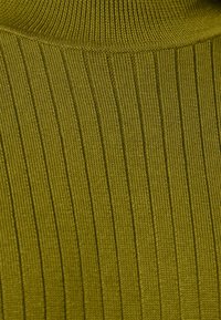 Olivově zelená žebrovaná pletenina s vysokým límcem. Textura má vertikální pruhy a hladký povrch. Detailní záběr zdůrazňuje detaily.