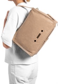 Beige leren rugzak met een gestructureerde vorm, voorzien van een ritsluiting, zichtbare stiksels en een ruitpatroon ventilatiedetail op de achterkant.