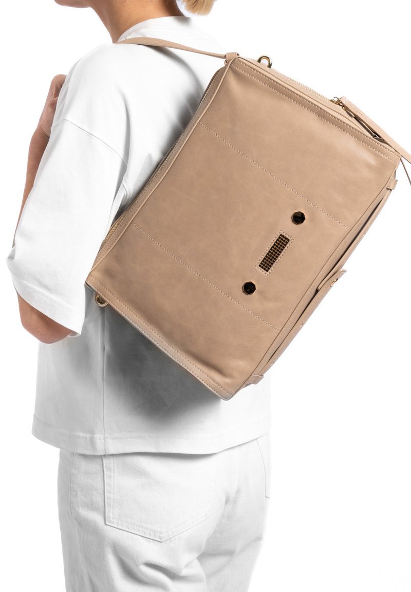 Beige leren rugzak met een gestructureerde vorm, voorzien van een ritsluiting, zichtbare stiksels en een ruitpatroon ventilatiedetail op de achterkant.