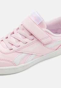 Lyserød lædersneaker med hvide accenter, snørebåndsdesign og en velcrostrop. Textureret overflade med polstret krave for komfort.