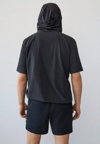 Camisa negra de manga corta con capucha, con una textura suave, combinada con pantalones cortos oscuros. Diseño minimalista con un ajuste relajado.