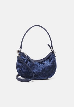 Petit sac à main en forme de croissant en velours froissé bleu foncé avec deux poignées assorties et ferrures argentées sur fond blanc.