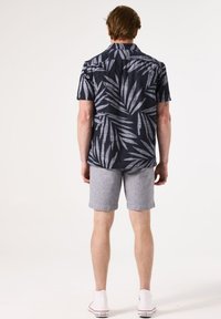 Camisa de manga corta en color navy con un patrón de hojas en gris claro, combinada con pantalones cortos gris claro y zapatillas blancas, vista desde atrás.