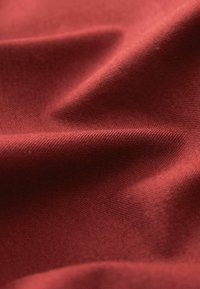 Tissu texturé d'un rouge profond, présentant une surface lisse avec de subtiles plis. Le matériau semble durable et tissé.