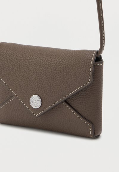 Καφέ δερμάτινη τσάντα χιαστί με ραφές σε λευκό χρώμα και στρογγυλό ασημένιο κούμπωμα, διαθέτει λεπτό λουράκι.