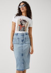 Tricou grafic alb cu un pisoi purtând ochelari și o eșarfă roșie, asortat cu o fustă creion din denim albastru deschis, cu două buzunare în față.