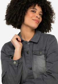 Veste en denim gris avec un devant à boutons, deux poches poitrine et des boutons à motif étoile. Présente un col et une légère décoloration.