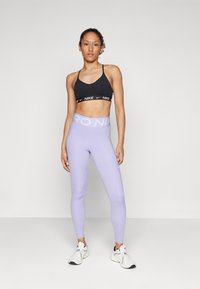 Un top sport negru cu bandă logo, asortat cu colanți de un violet deschis cu talie lată și logo. Pantofii sport albi completează look-ul.
