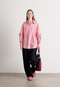 Pink striped button-up shirt with oversized sleeves, paired with loose black pants and pink shoes. A maroon bag is carried on one arm.