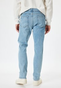 Jeans de mezclilla azul claro con un corte ajustado, diseño de cinco bolsillos y detalles en el yugo trasero. Combinados con calzado blanco.