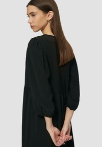 Schwarzes Kleid mit rundem Ausschnitt, Puffärmeln und geraffter Taille. Glatter Stoff mit fließender Silhouette. Einfaches Design.