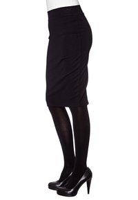 Musta kynähame joustavasta kankaasta, jossa on keskikorkea vyötärö ja sileä tekstuuri, yhdistettynä mustiin korkokenkiin ja läpinäkymättömiin sukkahousuihin.