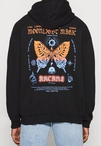 Felpa nera con cappuccio caratterizzata da una grande grafica sul retro con una farfalla, elementi celesti e testo in arancione e blu. Tessuto morbido, vestibilità casual.