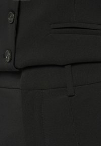 Zwarte op maat gemaakte suit met een soepele textuur, voorzien van een knoopsluiting en een zijzakdetail op de broek, wat zorgt voor een samenhangende uitstraling.