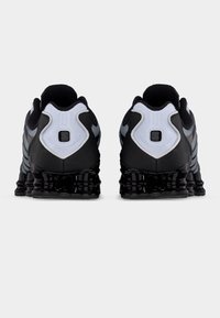 Ζευγάρι μαύρων και γκρι αθλητικών παπουτσιών που δείχνουν την πίσω πλευρά με επενδυμένους γιακάδες και λεπτομερή, υφή στο πέλμα, σε λευκό φόντο.