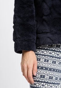 Marineblått fluffigt jacka med mjuk textur och avslappnad passform, tillsammans med mönstrade leggings med snöflinge- och hjärtmotiv.