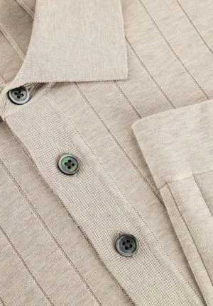 Beige geribbelde gebreide cardigan met een kraag, drie zichtbare donkere knopen en een omgeslagen manchetknoop aan de mouw.