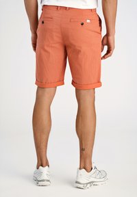 Pantaloni corti a scacchi arancioni con risvolti, dotati di due tasche posteriori con bottoni neri e un piccolo etichetta con logo sulla tasca destra.