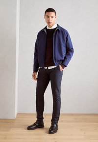 Chaqueta bomber navy sobre un suéter burdeos, combinada con pantalones oscuros y zapatos negros, presenta un cuello en contraste y un corte a medida.