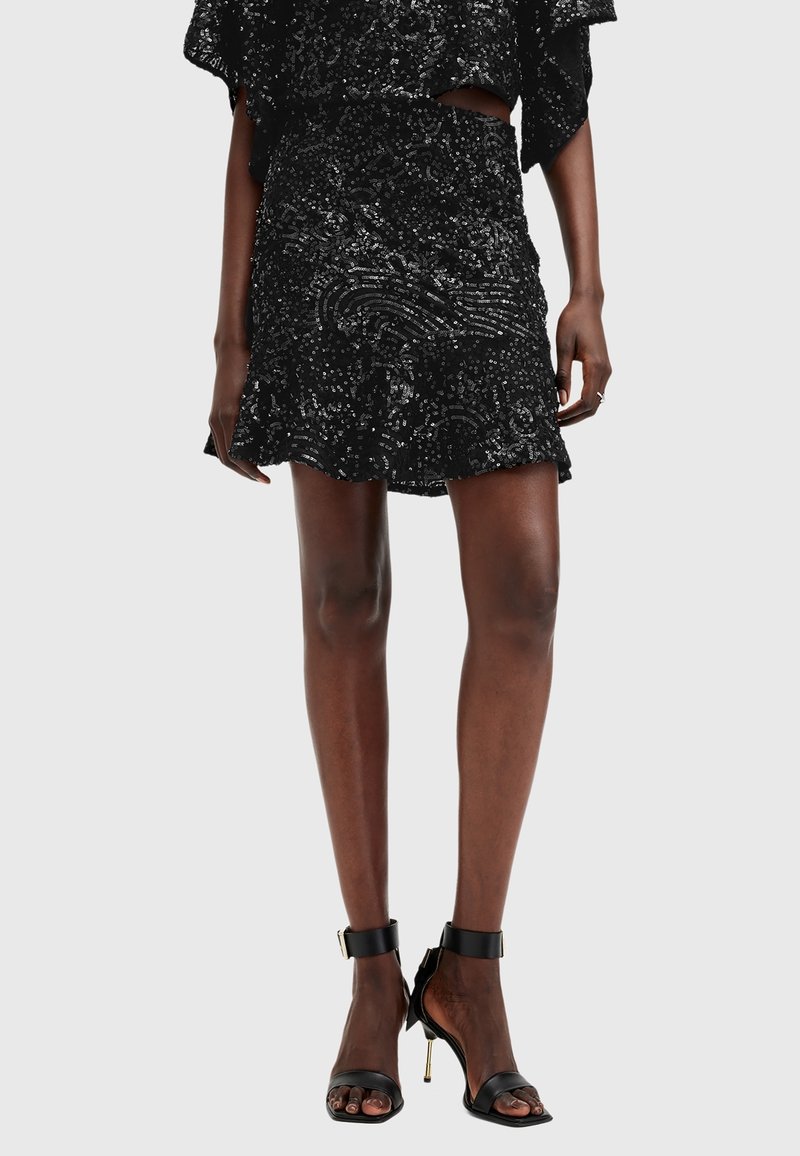 Femme portant une jupe noire à sequins avec des motifs ondulés et des sandales noires à talons hauts avec des brides à la cheville.