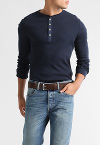 Camisa henley de manga larga en navy con textura acanalada y tapeta de cinco botones, combinada con jeans de mezclilla azul claro y un cinturón de cuero marrón.