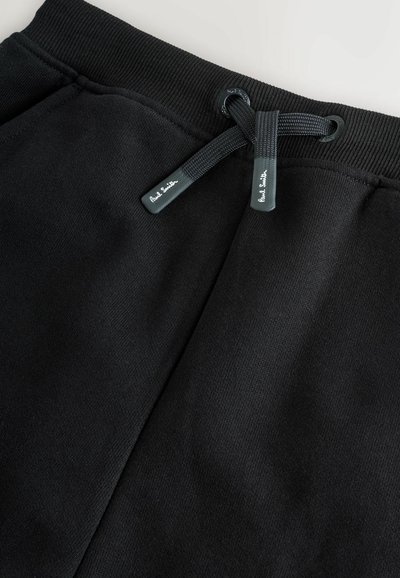 Mustat collegehousut, joissa on tekstuuri pinta, varustettuna ribbeillä vyötäröllä, nyörikiinnityksellä ja logotägeillä vyötärön lähellä.