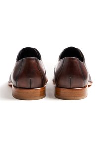 Braune Lederschuhe mit polierter Oberfläche, abgerundetem Zehenbereich und kleinem Absatz. Auffällige Nahtdetails entlang der Rückseite und Seiten.