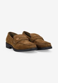 Mocasines de ante marrón con detalle de costura y un botón decorativo. Suela de goma negra plana. Diseño de punta ligeramente afilada.