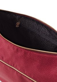 Roter, strukturierter Handtascheninnenraum mit schwarzem Innenfutter. Goldfarbener Reißverschluss und eine kleine Reißverschlusstasche sind sichtbar.