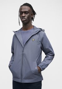 Lightweight, hooded jacket in grey fabric. Features a zip closure, elastic cuffs, and a small embroidered logo on the chest.