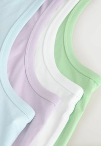 Quatre débardeurs pliés en bleu pastel, lavande, blanc et vert empilés sur une surface blanche montrant les encolures et les bords.
